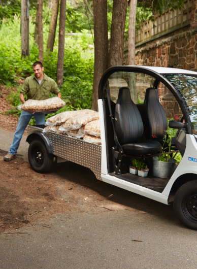 A man unloading mulch from an electric vehicle truck bed in the park
