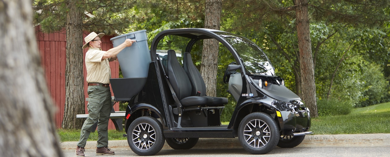 A groundskeeper loading a gray garbage can into a black electric vehicle